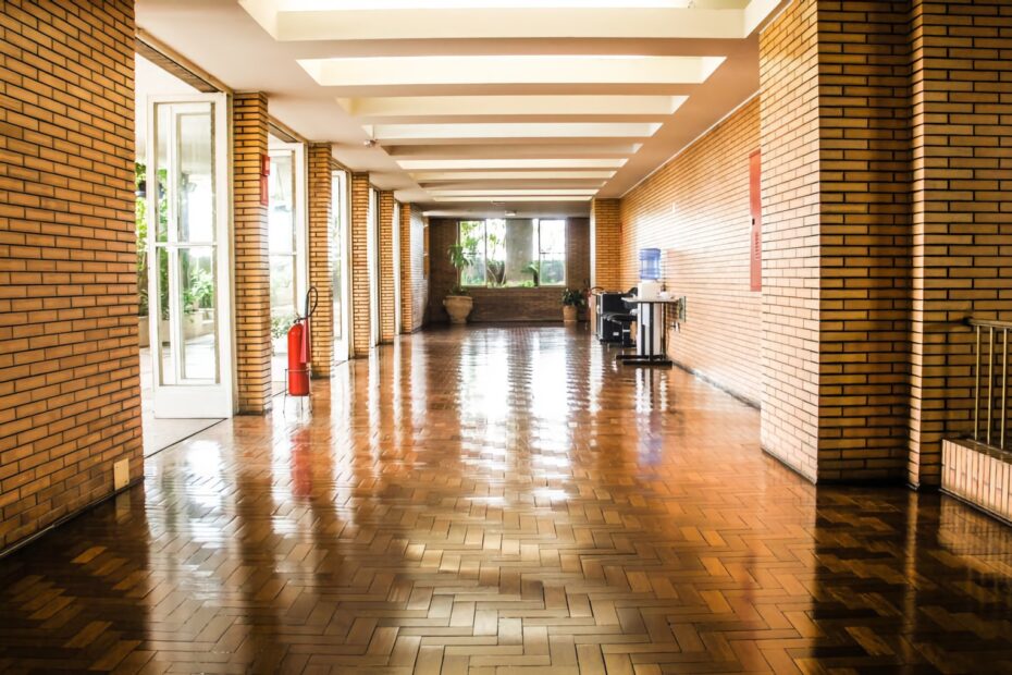 Long hallway with shiny parquet flooring, brick walls, and large windows leading to an outdoor area.